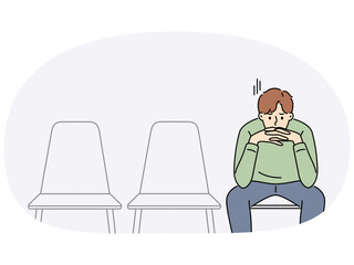 Sad man is waiting for start of interview, sitting in office corridor with empty chairs. Guy is nervous before interview because of problems in labor market and difficulty of finding well-paid job