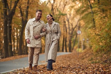 Smiling, hawing a walk. Lovely couple are together in the autumn forest near the road