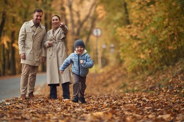 Fototapeta premium Running, having fun. Happy family are together in the autumn forest near the road