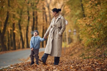 Fototapeta premium Mother with her son are having a walk in autumn forest near the road