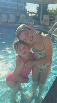 4K: Two young girls smiling at the camera lying on an Inflatable Lilo in the Swimming pool on Vacation Holiday. Vertical Video. Stock Video Clip Footage
