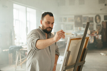 Male artist painting on canvas in a sunlit art studio