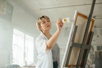 Young female artist working on a painting by the window