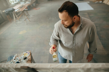 Overhead shot of a male artist painting on a canvas in his workshop.