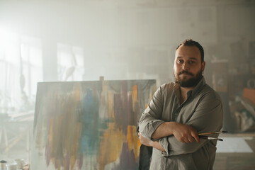 Portrait of a male painter in a creative workspace with abstract art in the background