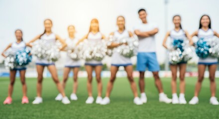 Obraz premium Blurred cheerleading team with pom poms on green field in sunshine