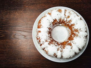 Delicious pumpkin cupcake sprinkled with powdered sugar on a white plate on a dark wooden table