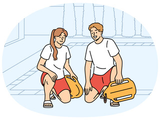 Obraz premium Pair of lifeguards sit by pool at hotel, holding swim training aids and keeping visitors safe. Smiling lifeguards or trainers working in fitness club urging people to visit swimming sports center