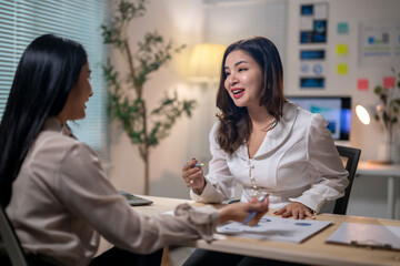 Fototapeta premium Two women are sitting at a desk, talking to each other