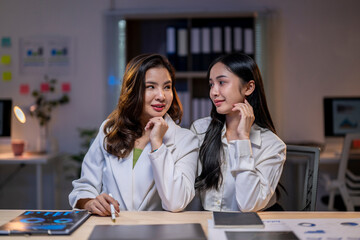Two women are sitting at a desk with a computer monitor in front of them