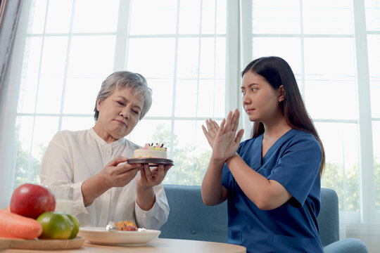 Unhappy Asian senior woman wants to eat cake bakery but stop by nutritionist. Female medical nurse forbidding elderly grandma to eat sweet dessert. Doctor gives advice to mature on improving diet.