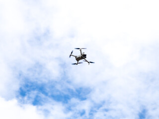 Flying drone on blue sky background. Modern white UAV drone quadcopter with camera is being controlled to stay in the air.