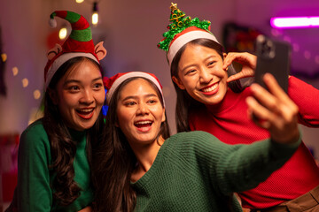 Three women are smiling and taking a selfie with a cell phone