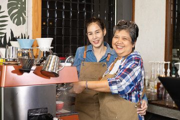 Young barista female hiring senior, elderly, 60s pensioner worker working in cafe bakery small business shop, two waitresses women standing behind coffee counter using technology cash register machine