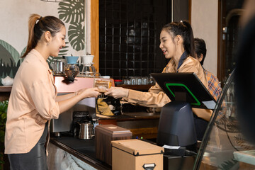 Young barista female hiring senior, elderly, 60s pensioner worker working in cafe bakery small business shop, two waitresses women standing behind coffee counter using technology cash register machine