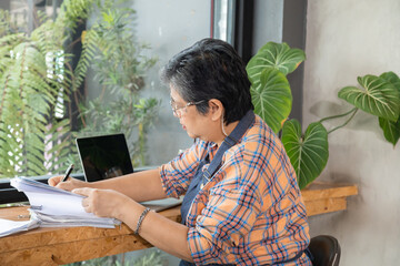 Senior barista female or employee concentrate on stacks of tax declaration bills, restaurant owner...