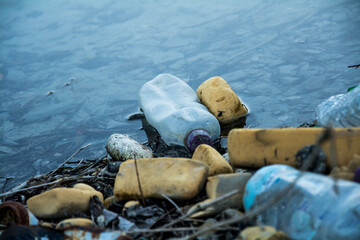Fly tipped rubbish with the focus on a generic empty drinks bottle floating in the water. Represents environmental issues such as plastic pollution in the UK and the world. Sign of degradation.