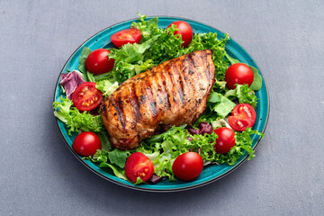 Grilled chicken breast ( fillet ) with lattuce salad and cherry tomatoes . Top view