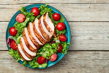 Grilled chicken breast ( fillet ) with lattuce salad and cherry tomatoes . Top view