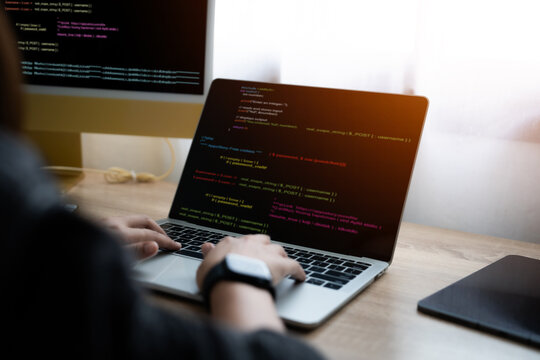 A person is typing on a laptop computer with a colorful screen. The laptop is open to a page with a lot of code on it. The person appears to be focused on their work