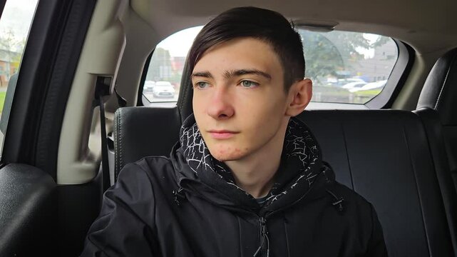 Teenage Boy Looking Thoughtfully From Backseat of Car on Overcast Day While Traveling Through City. Fourteen years old boy inside vehicle at town car trip