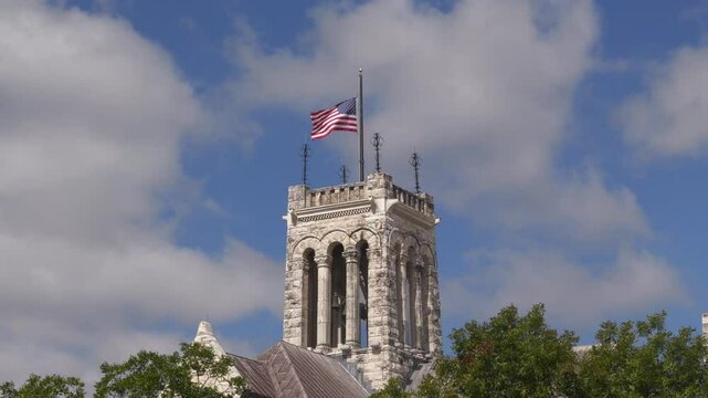 American flag on top of Comal County Courthouse in New Braunfels, Texas with cloudy sky background