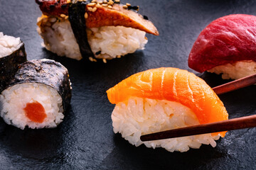 Sushi assortment on a black background. Salmon nigiri with chopsticks and other sushi and rolls