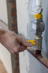 Male hand turns off yellow gas tap on a gas boiler. Closeup.