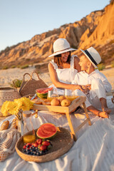 A joyful mother and son share a picnic on a sandy beach during sunset. The warm atmosphere creates...