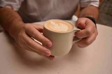 Close-up of male hands with a steaming cup of cappuccino — rich aroma and a moment of comfort.