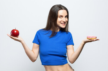Beautiful young woman having to choose in between a donut and a red apple. On white background