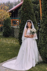 A woman in a white dress is holding a bouquet of flowers. She is standing in front of a bush