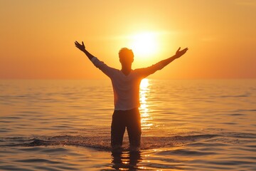 Fototapeta premium A silhouetted man raises arms in the ocean against sunset glow, evoking freedom and connection to nature's grandeur.