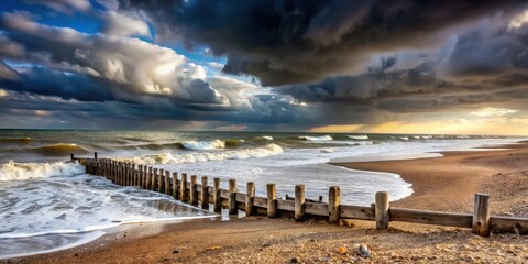 A wooden seawall stretches across the sandy beach, with crashing waves and stormy clouds creating a dramatic seascape.