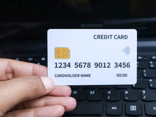 Hand holding credit card over a laptop keyboard, symbolizing digital payment and finance