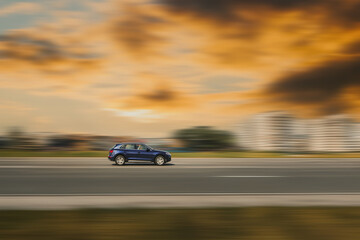 Car on Road. A blue car is driving down an asphalt street with a blurred background from speed. Wallpaper with a car on orange clouds in the background