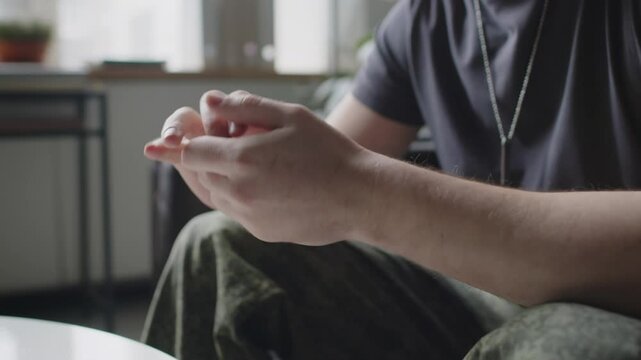 Close-up shot of unrecognizable male soldier in military uniform nervously wringing his hands during therapy session in office