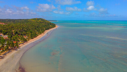 Aerial view of Jarapatinga Beach, Alagoas, with calm green and blue waters, golden sand, and surrounded by lush vegetation, creating a paradisiacal seaside retreat in Alagoas, Brazil.