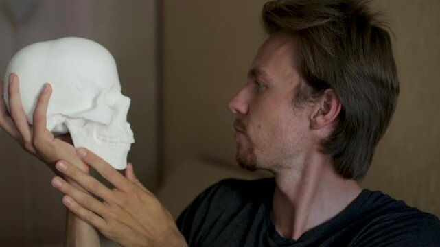 Man showing human skull replica to camera, concept of anatomy, halloween, death, education