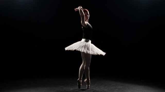 Dramatic and elegant dance of beautiful ballerina in darkness, slow motion shot. Graceful ballet dancer dancing alone on stage with bright soffit, female silhouette in contour light, classical art