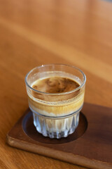 Dirty coffee on a wooden table; layered drink with a distinct robust espresso layer on the top and chilled cold milk or cream at the bottom.