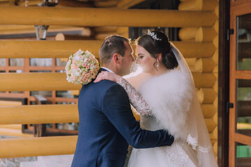 A bride and groom are hugging each other in front of a wooden door. The bride is wearing a white dress and a veil, while the groom is wearing a blue suit. The scene is intimate and romantic
