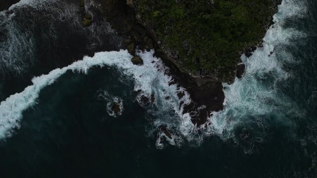 4k video footage - Aerial view of Watu Karung Beach, Pacitan, East Java, Indonesia with crashing waves during cloudy day. Cape with cliffs by the sea and green plants around at tropical island