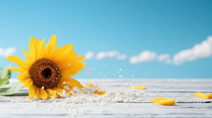 A bright yellow sunflower rests on a wooden surface against a clear blue sky with fluffy clouds, representing nature's beauty and simplicity in a serene scene.