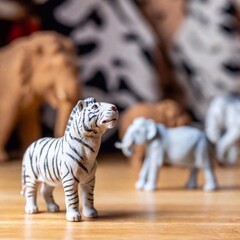 Naklejka premium Set of toy animals figurines, focusing on a tiny lion with other animals like elephants and zebras blurred in the background