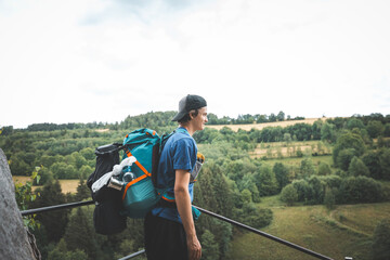 Hiker with a blue backpack carefully ascends metal stairs surrounded by moss-covered rocks and dense greenery, navigating a rugged forest trail in the Beskydy Mountains