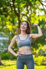 Asian woman showing bicep in activewear at outdoor park. Confident young female embracing strength...