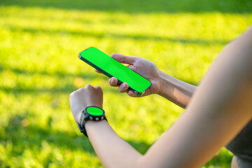 Close-up of Asian woman using smartphone and smartwatch for fitness tracking in outdoor park