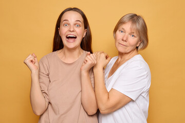 Two women celebrating joyfully together against a bright yellow backdrop, expressing happiness and connection, showcasing a moment of shared excitement