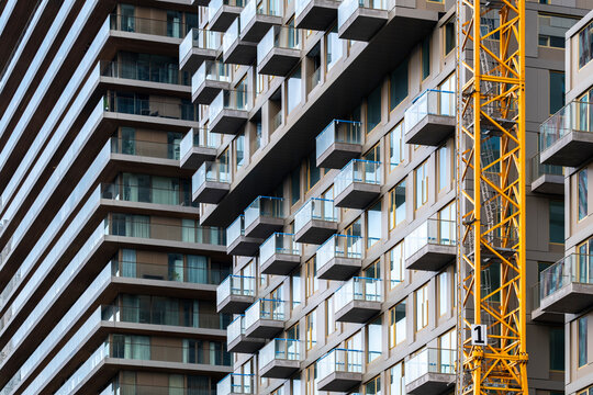 The image features a towering high-rise building, where numerous balconies extend outward, accompanied by a bright yellow crane indicating ongoing construction work in Rotterdam